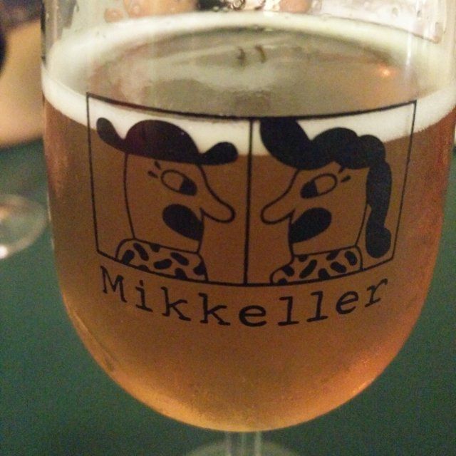 A tulip-style glass of yellow/amber beer with a light head atop a green table