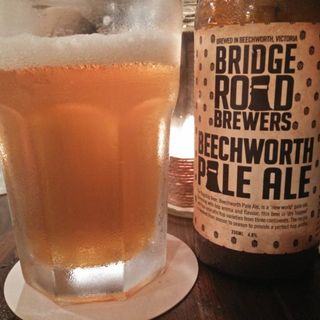 A photo showing this beer’s foamy, light head and the bottle it came from, illuminated by a candle