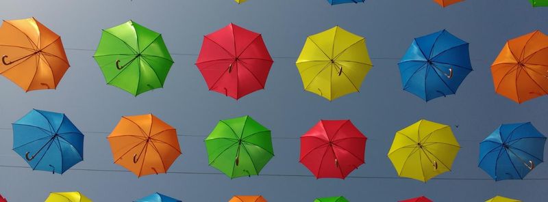 a photograph looking upwards at many umbrellas of varying colours, arranged in columns and rows